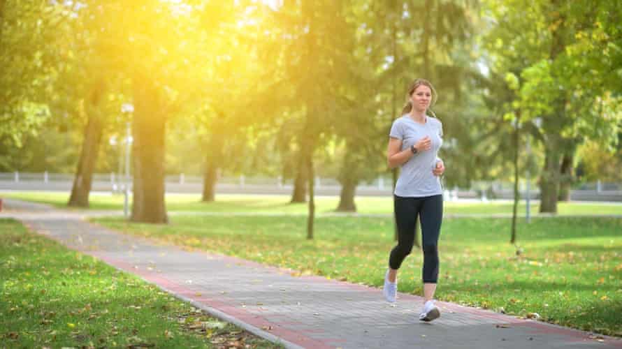 A woman running in the park with the sun rising behind her